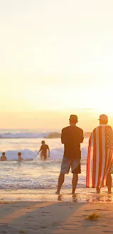 People enjoy a sunset at the beach as waves roll in and a man carries an American flag.