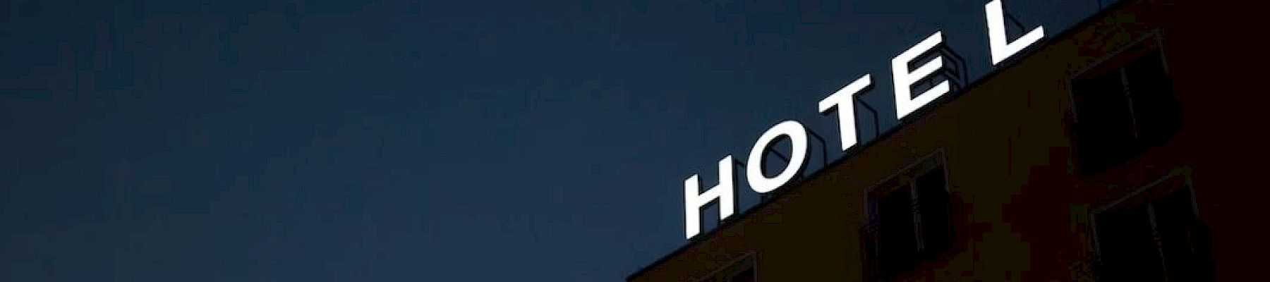 A hotel building at dusk with a large illuminated &ldquo;HOTEL&rdquo; sign across the roofline, set against a dark blue sky.