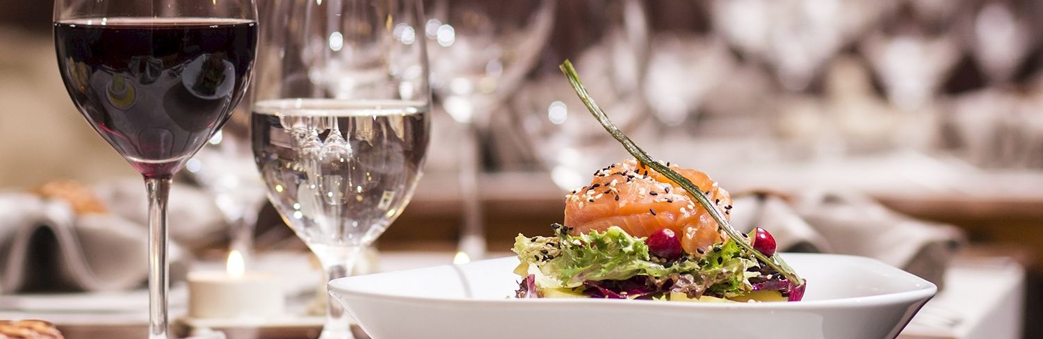 A refined dining setup with red wine, water glass, and a plated salad-topped burger centerpiece on a white table, ready for service.