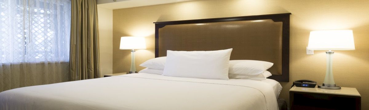 A hotel-style bedroom with a made bed, nightstands, table lamps, curtains, and a ceiling fan.