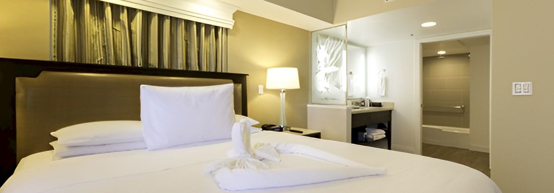 A modern hotel room featuring a king-size bed with white linens, pillows, bedside lamps, and curtains.