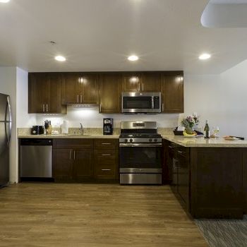 A contemporary kitchen with dark wood cabinets, stainless steel appliances, a center island, and a small dining area in the background.
