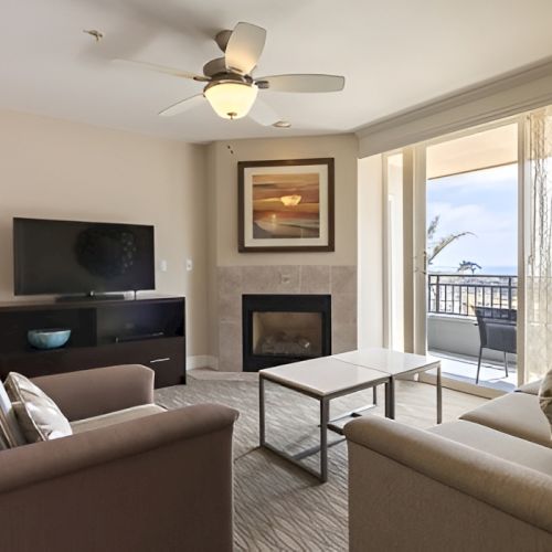 A modern living room with a sofa set, a coffee table, a wall-mounted TV, a fireplace, artwork, and a balcony view through sliding doors, ending with period.