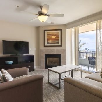 Modern living room with a fireplace, TV stand, beige sofas, coffee table, and a balcony view. Bright, cozy, and inviting.