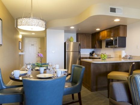 A modern, open-concept kitchen and dining area with a round table, blue upholstered chairs, stainless appliances, and warm lighting.