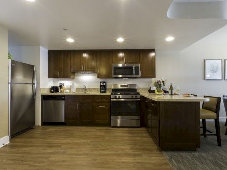 A modern kitchen with dark wood cabinets, stainless steel appliances (refrigerator, oven, microwave), and a breakfast bar island. Top it at 140 characters, always ending the sentence.