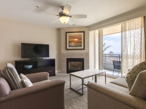 A cozy living room with a sofa set, a wall-mounted TV, a fireplace, a coffee table, and a balcony view through glass doors.