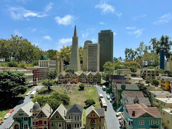 A miniature cityscape with colorful row houses in the foreground and modern high-rises in the background under a clear blue sky.