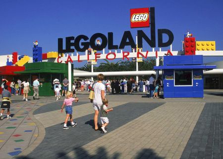 A virtual LEGO city scene with people walking outside Legoland, colorful buildings, and a bright entrance in the background.