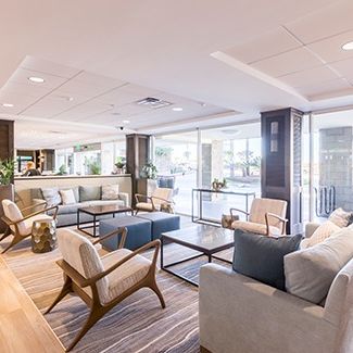 A bright, modern living room with a large window, white walls, a cozy sofa, coffee table, plants, and warm lighting.