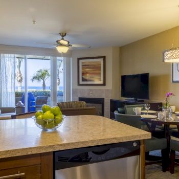 A modern living space with a kitchen island, dining area, sofa seating, wall art, a TV, and a sliding glass door to a balcony.